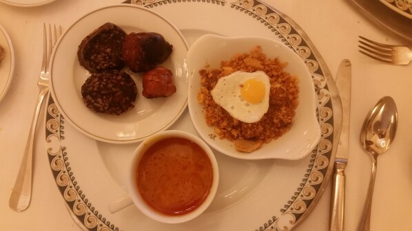 Un plato con un huevo frito, salchicha y un bol de salsa roja.