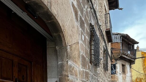 Un edificio de piedra con una puerta de madera y un pequeño ventanal con una reja de metal.
