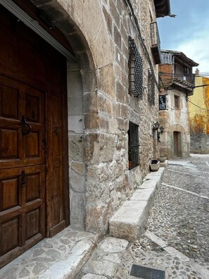 Un edificio de piedra con una puerta de madera y un pequeño ventanal con una reja de metal.