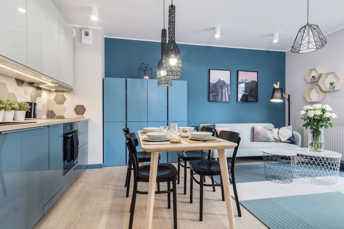 A modern kitchen with blue cabinets, a dining table set for four, and a blue sofa in the living area.