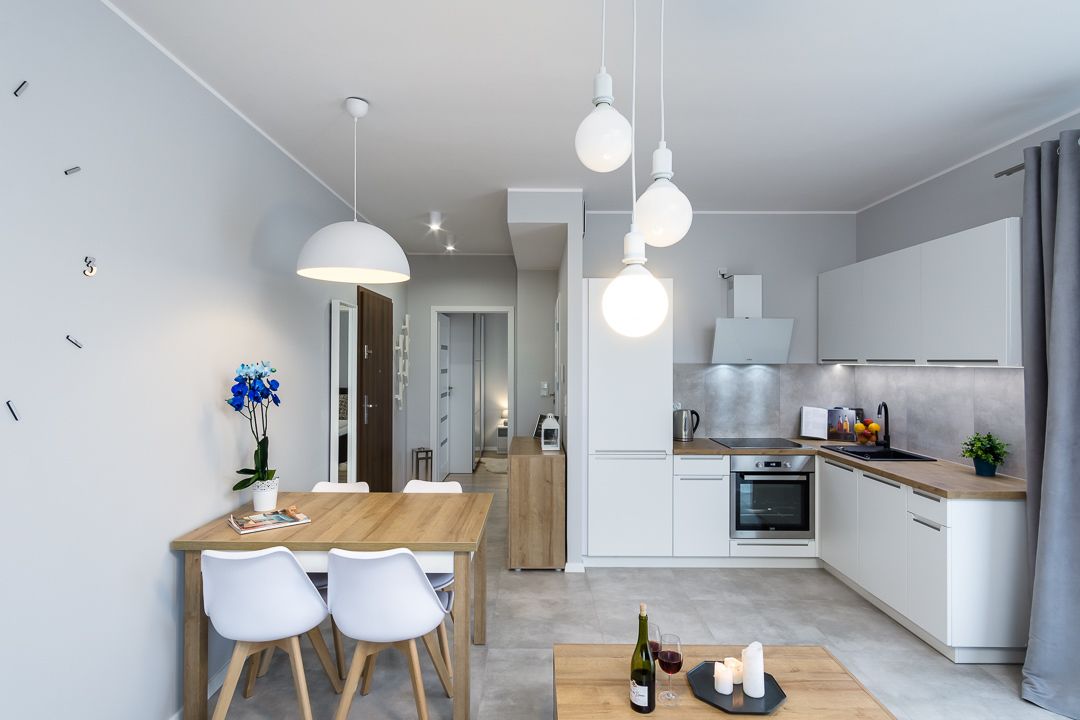 Une cuisine moderne avec des meubles blancs, une table à manger en bois et des luminaires suspendus.