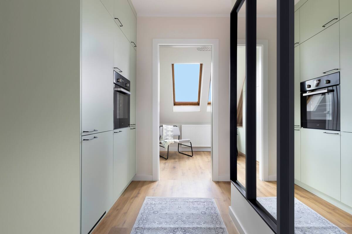 A modern kitchen with light green cabinets, a built-in oven, and a skylight.