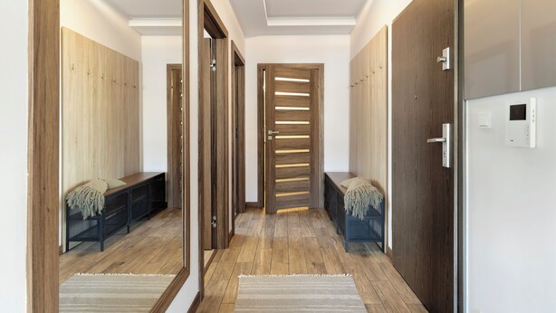 Un couloir avec un plancher en bois, un banc et un miroir sur le côté gauche.