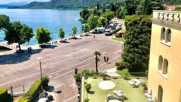 Un hotel con estacionamiento, zona de estar al aire libre y vistas a un lago y montañas.