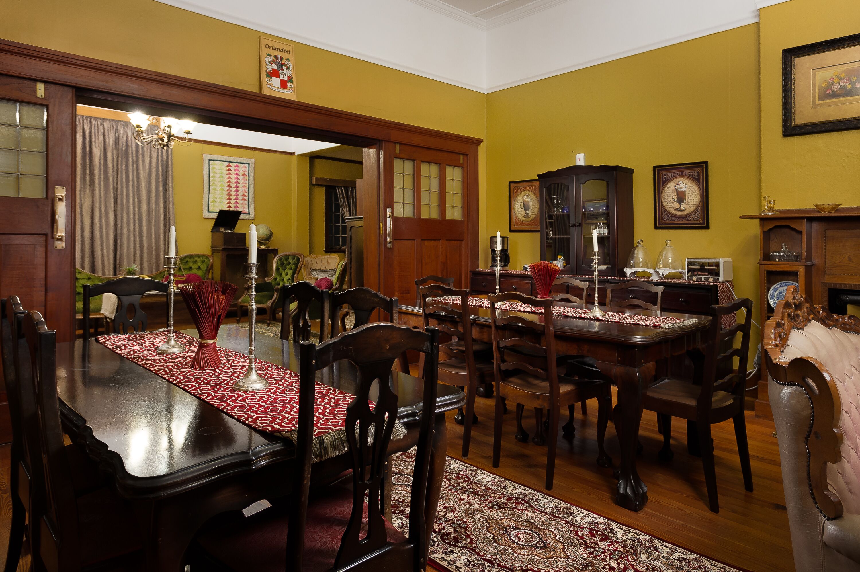 Une salle à manger avec une table et des chaises en bois, un chemin de table rouge et blanc à motifs, et un lustre.