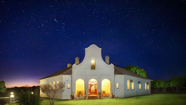 A large, white building with a central arched entrance and multiple windows, set against a starry night sky.