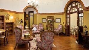 A room with wooden flooring, floral-patterned chairs, a round table with a brass object, and a chandelier.