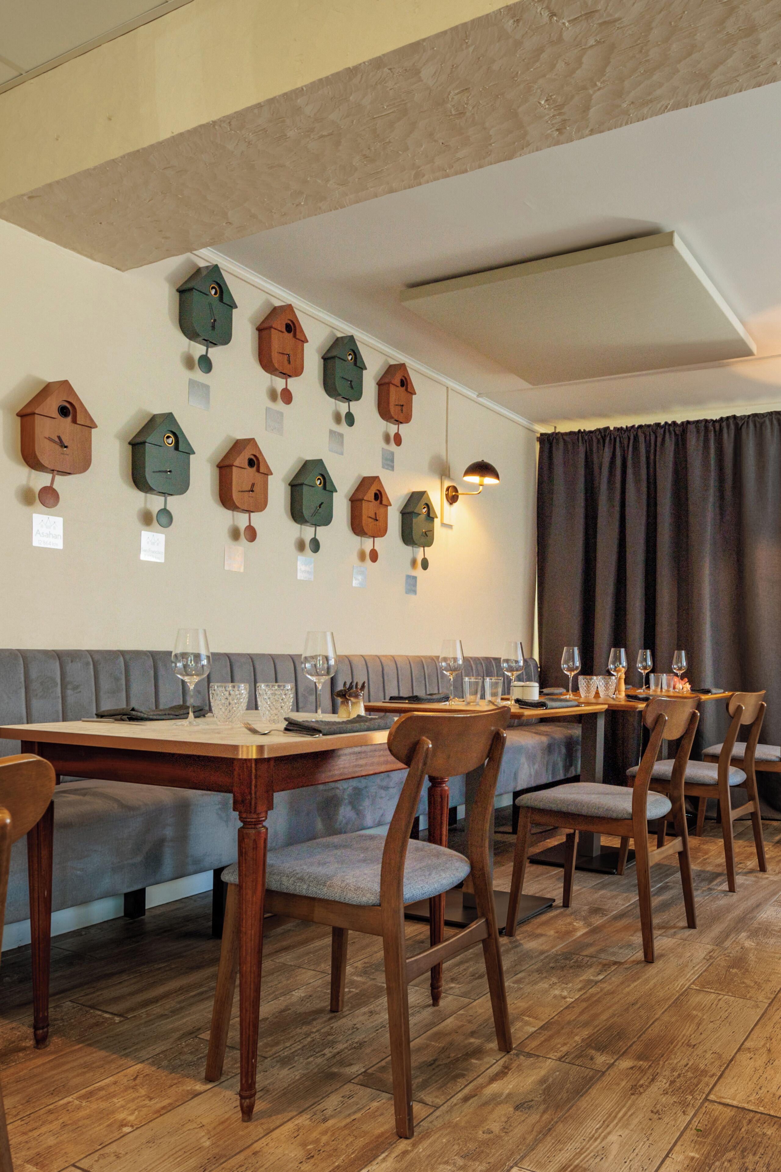 Un espace repas avec des tables et des chaises en bois, un canapé gris et des décorations murales représentant des nichoirs.