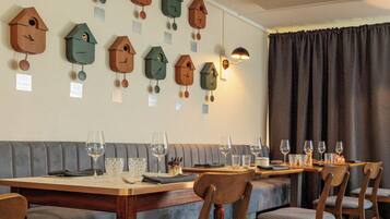 Un espace repas avec des tables et des chaises en bois, un canapé gris et des décorations murales représentant des nichoirs.