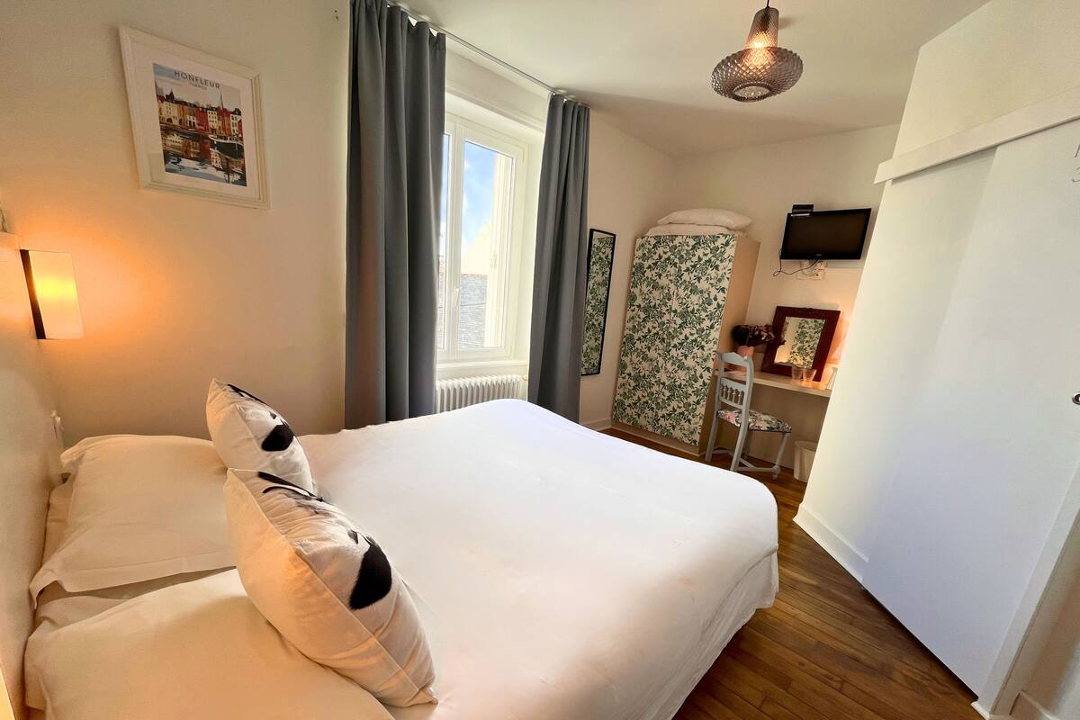 A hotel room with a large bed, a desk with a chair, a television, and a window with curtains.