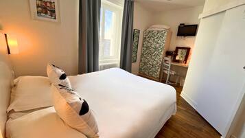 Quarto de hotel com uma cama grande, uma escrivaninha com cadeira, televisão e janela com cortinas.