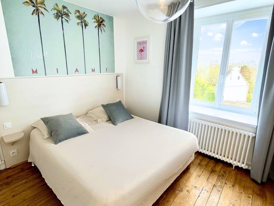 Un dormitorio con una cama grande, una lámpara de pared, una ventana con cortinas y una obra de arte en la pared.