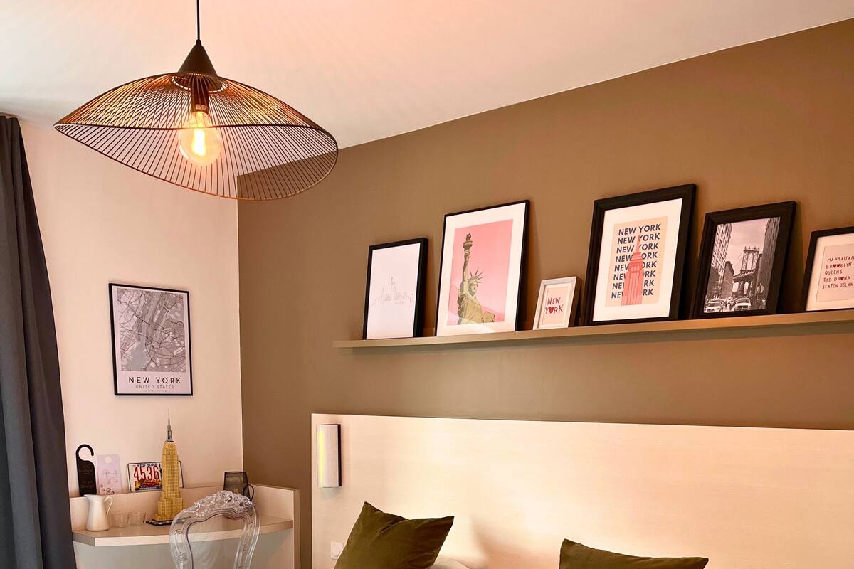 A hotel room with two beds, a nightstand, a shelf with framed pictures, and a hanging light fixture.