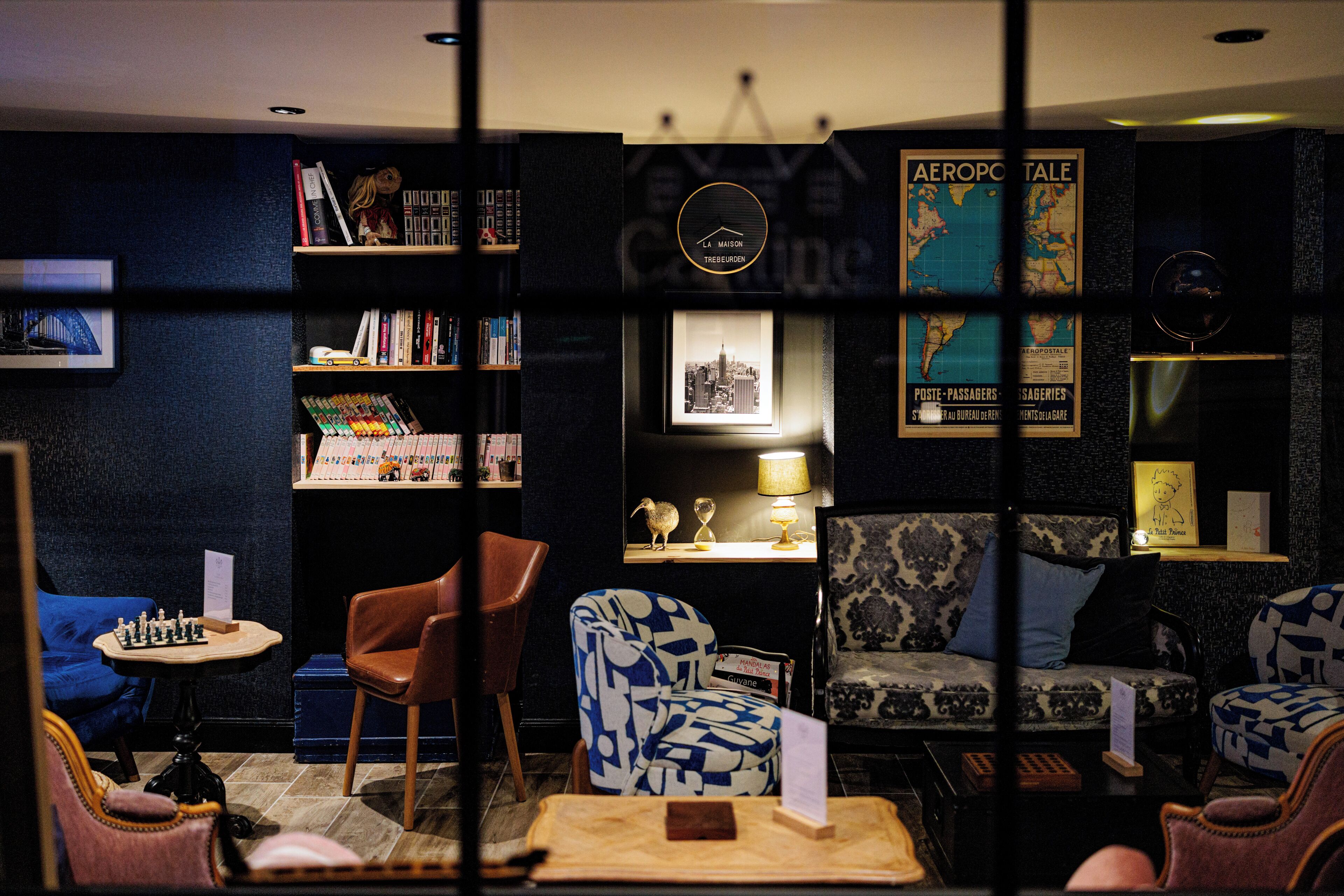 A cozy lounge area with a chessboard, comfortable seating, a bookshelf, and a map on the wall.