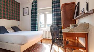 A bedroom with a bed, a desk, a chair, a radiator, and a window with curtains.