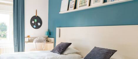 Un dormitorio con dos camas, un escritorio y una silla. Hay cuadros en la pared y un ventilador de techo.