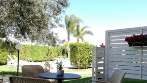 Ein Patio mit zwei Stühlen und einem Tisch, umgeben von Grünpflanzen und einem weißen Zaun.