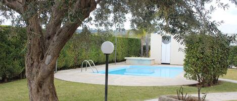 A backyard with a swimming pool, a large tree, and a stone planter.