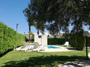 A pool area with lounge chairs and a small building, surrounded by greenery and a clear sky. - La Lantana (Ragusa)