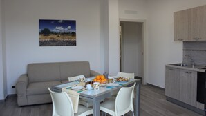 Ein moderner Essbereich mit Tisch für zwei Personen, einer Couch und einer Küche mit Holzschränken.