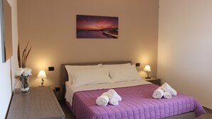 Ein Hotelzimmer mit einem Bett, zwei Nachttischlampen, einem Nachttisch, einer Vase mit Blumen und einem Bild an der Wand.