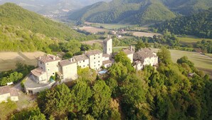 A medieval-style building complex with multiple structures, including a tower, surrounded by lush greenery and fields. - Agriturismo Castello della Pieve (Mercatello sul Metauro)