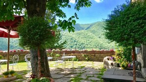 A patio area with stone flooring, potted plants, outdoor furniture, and a view of a forested hillside. - Agriturismo Castello della Pieve (Mercatello sul Metauro)