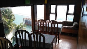 Un comedor con sillas y mesas de madera, un sofá y vistas al mar a través de amplios ventanales.