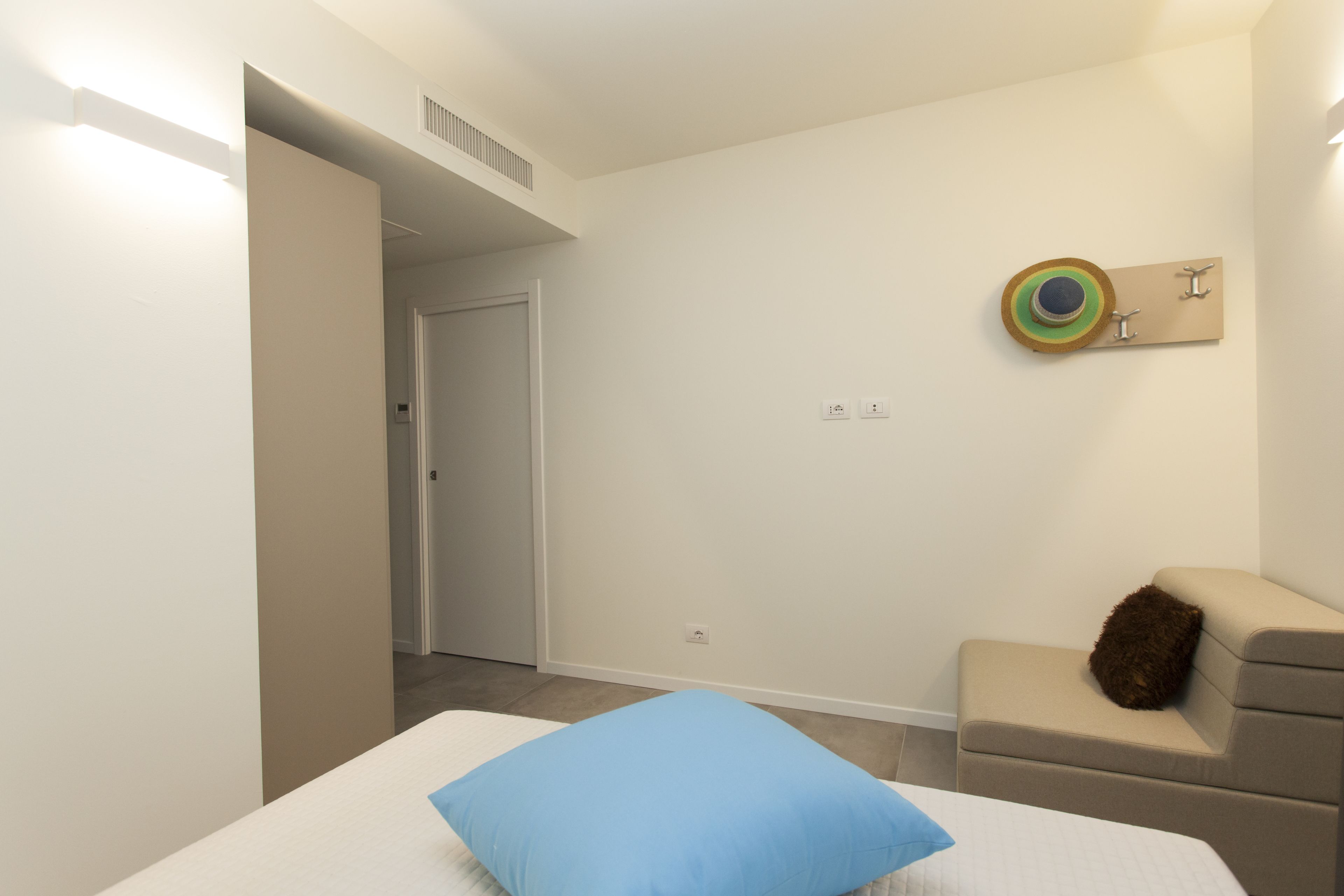 A modern bedroom with a bed, a small seating area, and a door leading to another room.