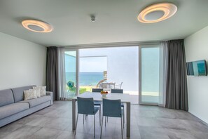 A modern living room with a sofa, dining table, and chairs, a balcony with a view of the sea, and a flat-screen TV mounted on the wall. - Residence Panama (Jesolo)