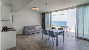 Una sala moderna con un sofá gris, una mesa de comedor con sillas y una zona de cocina con mostrador y armarios.