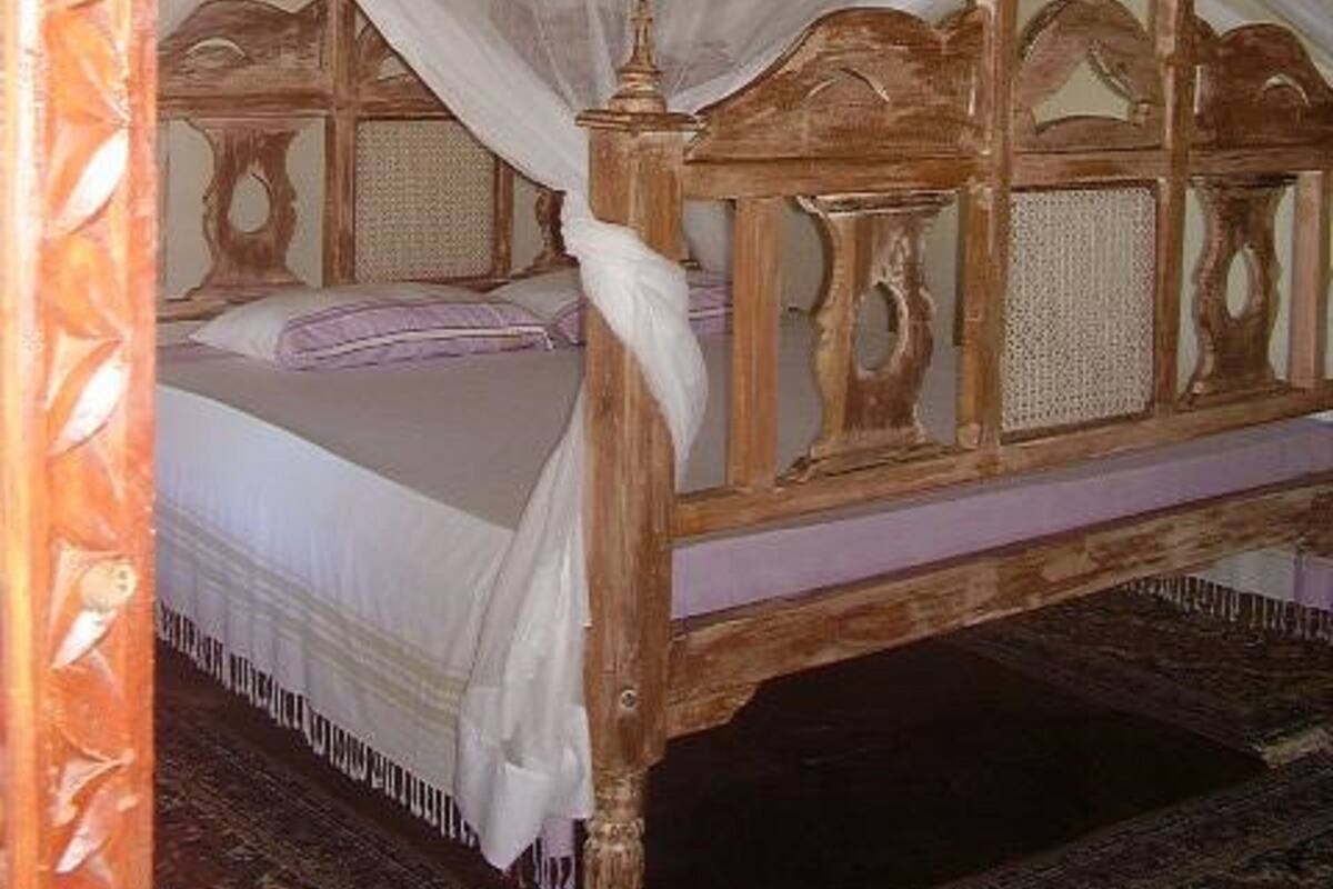 Una cama con dosel, un cabecero de madera y una alfombra estampada.