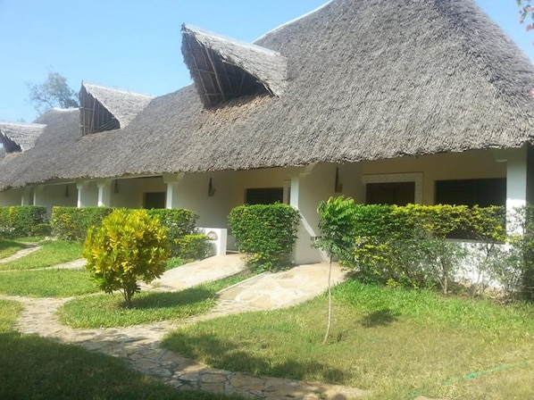 A row of thatched-roof cottages with a paved pathway leading to the entrance.