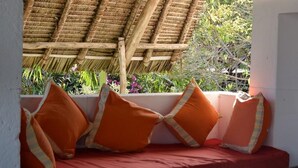 A window seat with red cushions and a thatched roof overhead.