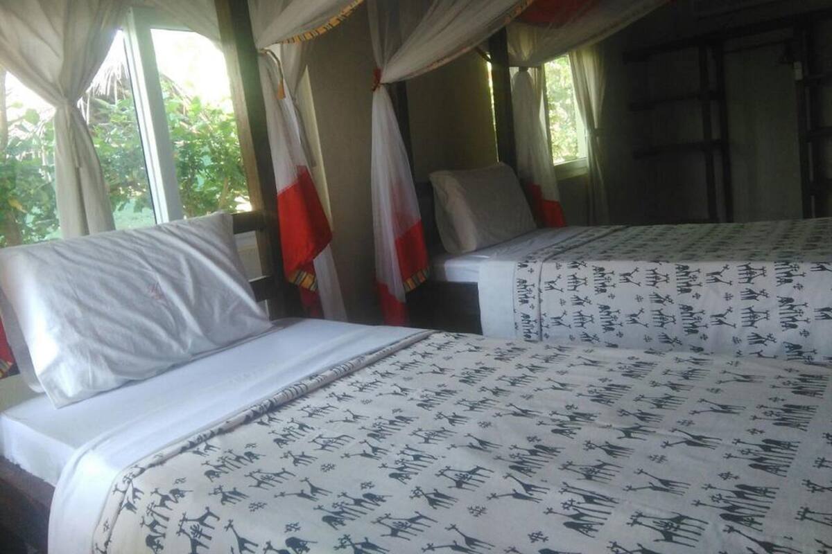 Habitación con dos camas, cada una con una colcha estampada, cortinas y vista a zonas verdes.