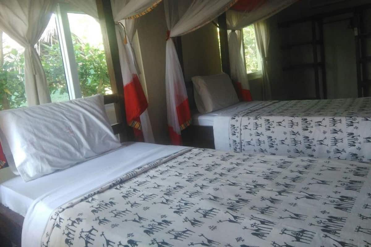 Habitación con dos camas, cada una con una colcha estampada, cortinas y vista a zonas verdes.