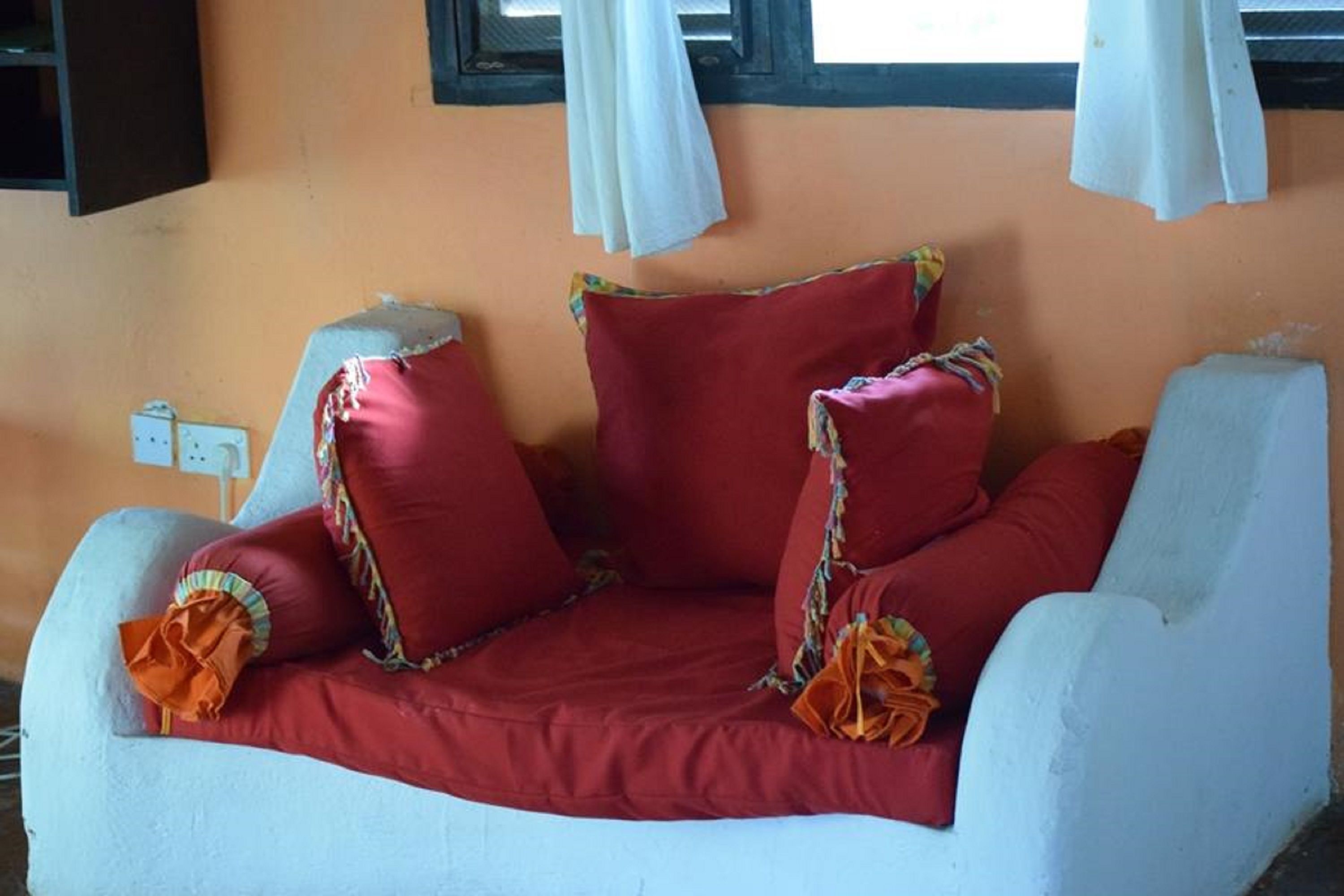 Un sofá blanco con cojines rojos y almohadones decorativos naranja frente a una pared color melocotón.