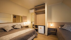 Et hotelværelse med en stor seng, et garderobeskab, et lille køleskab, sengeborde med lamper og et spejl.