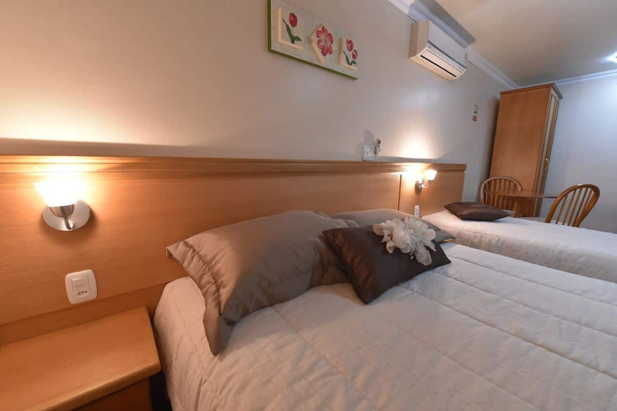 Ett hotellrum med två sängar, en sänggavel i trä, ett nattduksbord, en stol och en väggmonterad luftkonditioneringsanläggning.