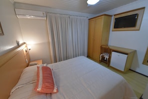Quarto com cama, escrivaninha, cadeira, guarda-roupa e ar condicionado.
