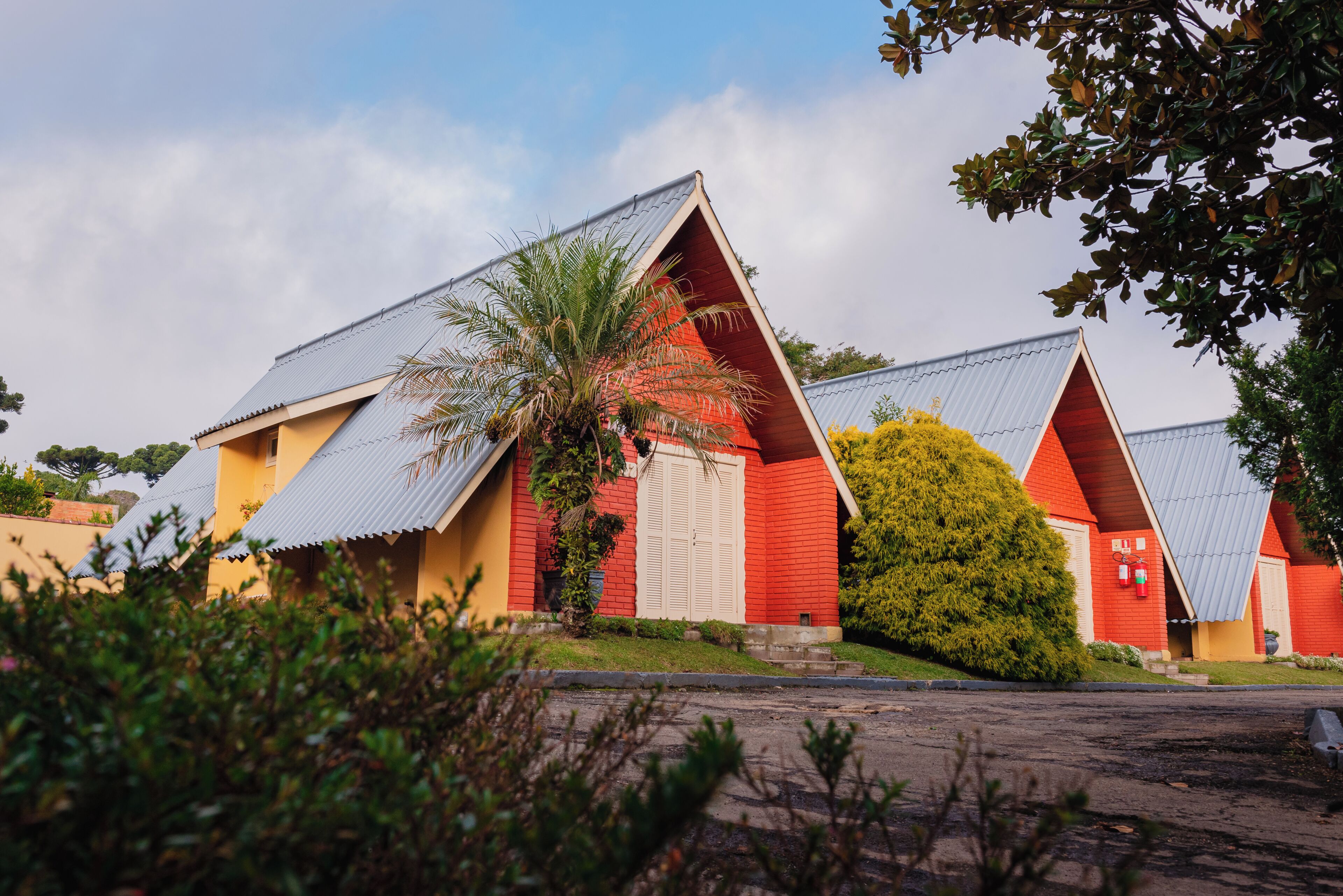 A building with a red facade and a sloped roof, surrounded by greenery.