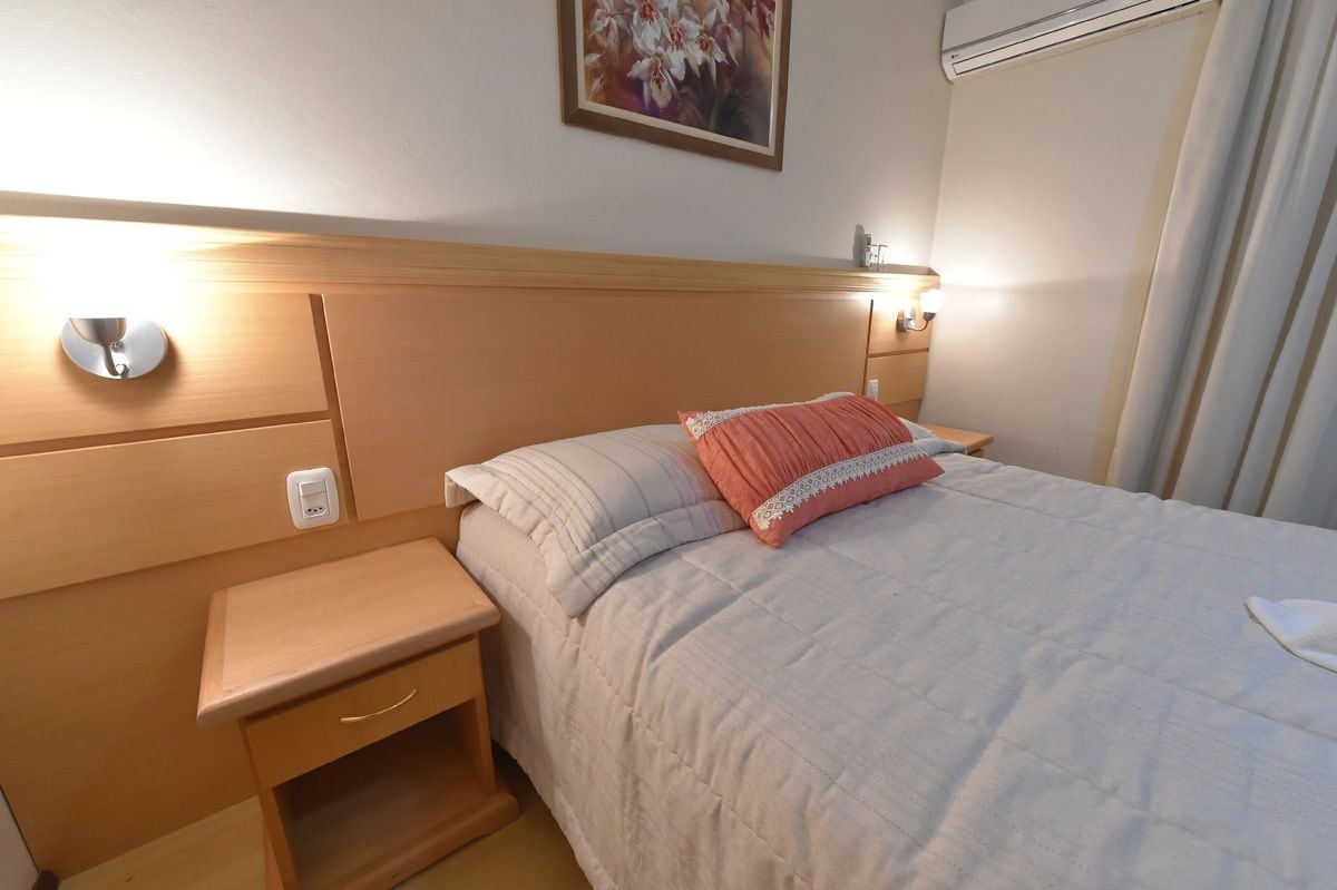 Une chambre d’hôtel avec une tête de lit en bois, une table de chevet avec une lampe et un lit recouvert d’une courtepointe et agrémenté d’un coussin décoratif.