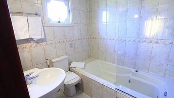 A bathroom with a bathtub, toilet, sink, and a window.