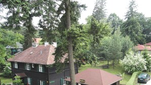 A two-story house with a red roof and green shutters, surrounded by lush greenery and a paved driveway. - Ośrodek Wypoczynkowy Bajka 3 (Lagow)