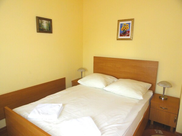 A neatly made bed with white linens, two bedside tables with lamps, and two framed pictures on the wall.