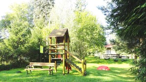 A playground with a wooden slide and climbing structure, surrounded by grass and trees. - Ośrodek Wypoczynkowy Bajka 3 (Lagow)