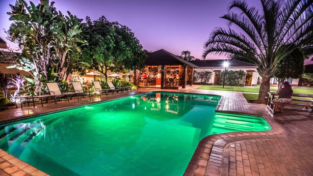Una piscina con borde de ladrillo, rodeada de sillas de descanso y palmeras.