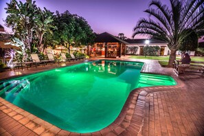 Una piscina con borde de ladrillo, rodeada de sillas de descanso y palmeras.