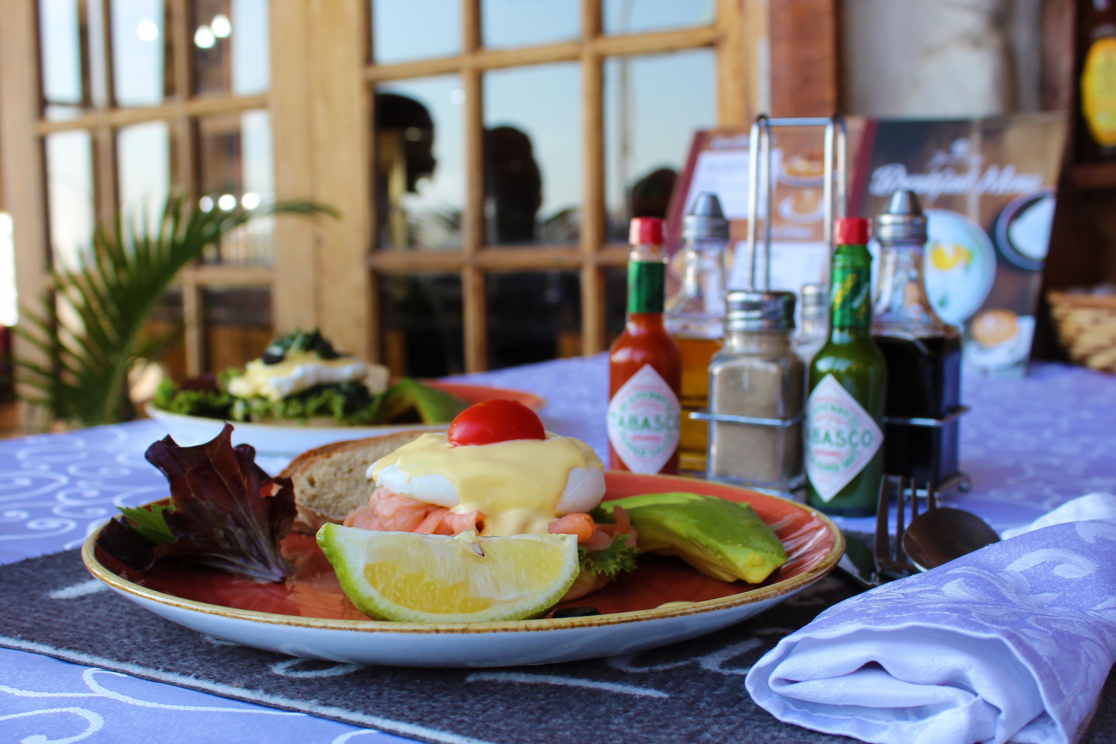 Un plato de comida con aguacate, tomate y un huevo pochado sobre una mesa, junto a una servilleta y aderezos.