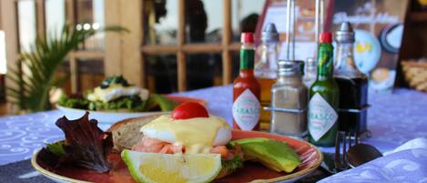 A plate of food with avocado, tomato, and a poached egg on a table with a napkin and condiments.